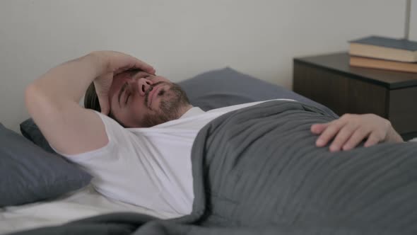Young Man Having Headache While Sleeping in Bed alt