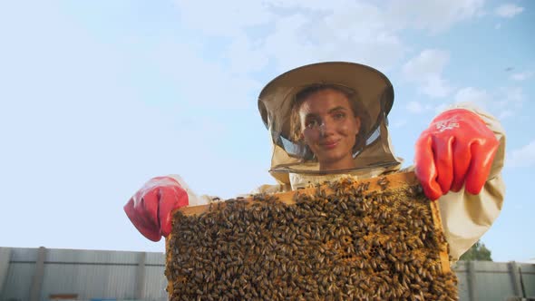 A Girl Beekeeper in a Protective Suit Carries a Frame with Honey From a Bee Hive