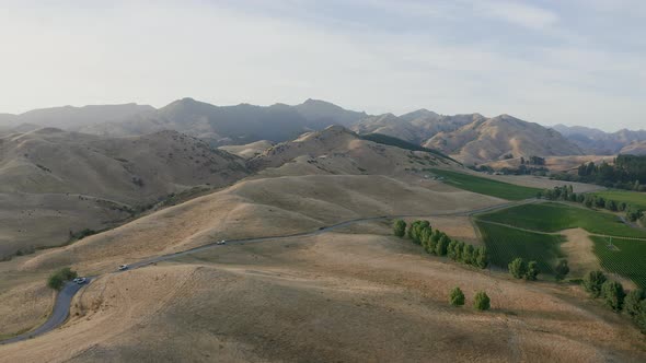 Aerial of dry hills in Marlborough as the vineyards bathe in the sun and three trucks drive along th alt