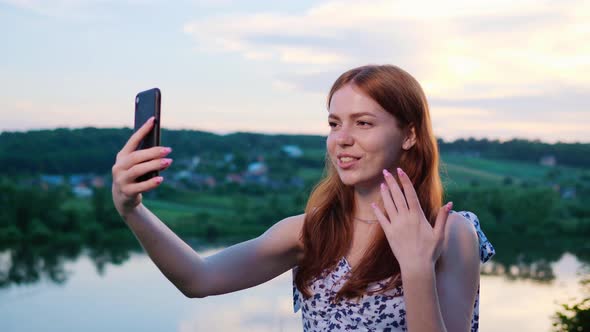 Ginger Woman Holding Camera or Mobile Phone in Hand and Makes Online Video Call alt
