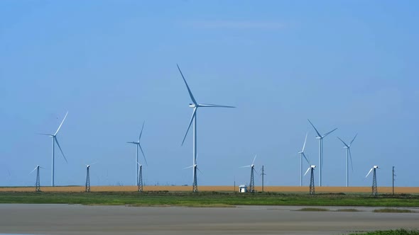 Wind Turbines with Blades for Generating Electricity Among a Yellow Field Against a Clear Blue Sky