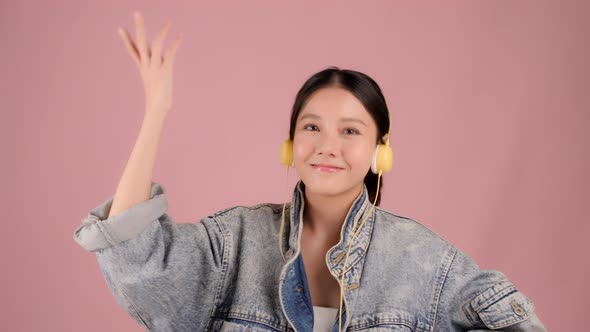 Pretty Asian girl listening music and dancing on pink background. alt