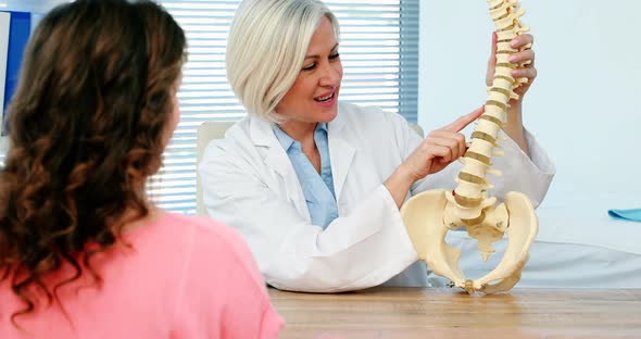 Female doctor explaining spine model to female patient alt