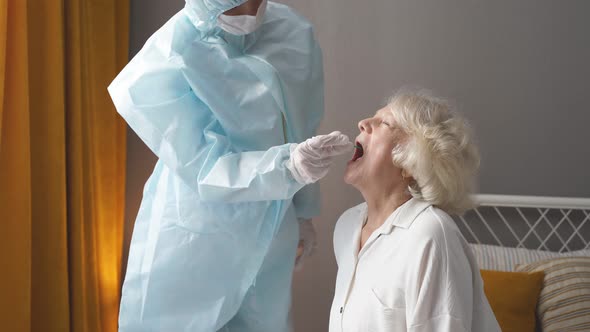 Doctor in Protective Suit Taking Throat and Nasal Swab From Elderly Female Patient to Test for