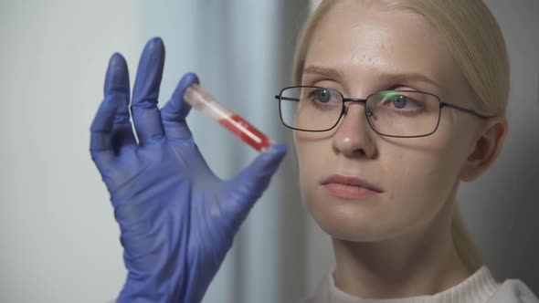 A Doctor in Strict Glasses Holds a Test Tube with a Blood Test