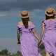 Young Twins Sisters in Purple Summer Dresses Walks Green Field Holding Hands - VideoHive Item for Sale