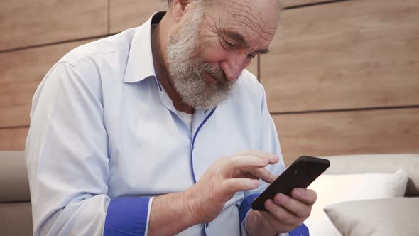 Happy bearded senior elderly 70s man user holding smart phone watching mobile video calling online l alt