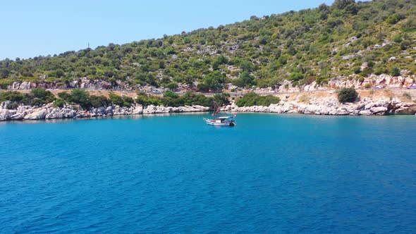 Aerial drone flying towards a sailboat anchored in the tropical blue Mediterranean Sea alongside a r alt