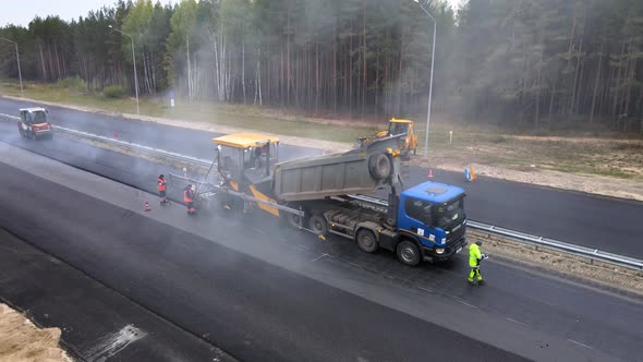 The final stage of road works. Laying the top layer of hot gray tarmac mix alt