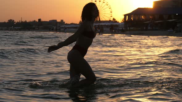 Jolly Brunette Girl in Bikini Throwing Water on River Bank in Slow Motion