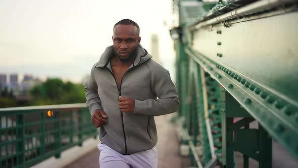 4K African man in sportswear and smart watch jogging on the bridge in the city alt