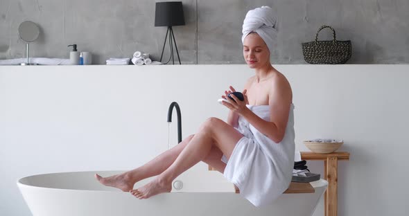 Delighted Halfnaked Pretty Woman White Bath Towels Applies Moisturizer to Her Legs Makes a Smoothing alt