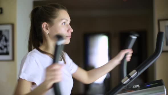 A young woman is training on an ellipsoid, holding on to leverage. Side view alt