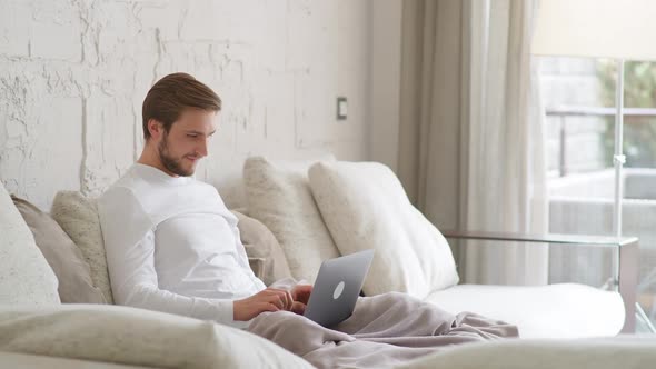 Cheerful Caucasian Man Sits at Home on the Couch and Works Using a Laptop Financial Manager on a alt