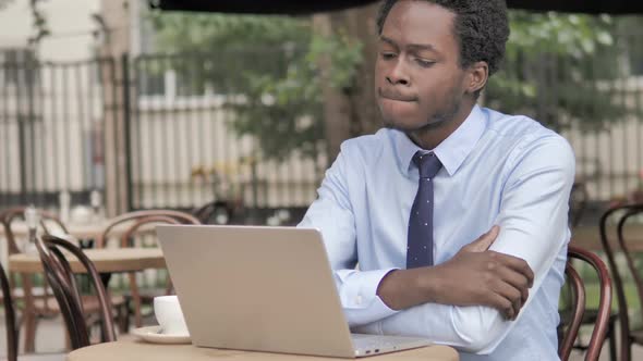 African Businessman Working on Laptop and Drinking Coffee in Outdoor Cafe alt