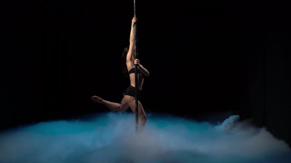 Girl with Flowing Hair Dancing on a Pole in a Dark Smoky Room. Black Background alt