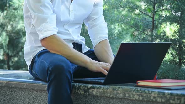 Student Sitting In Park And Typing On Laptop