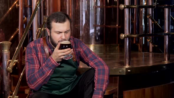 Professional Brewer in Apron Resting After Work, Drinking Beer of Own Production alt