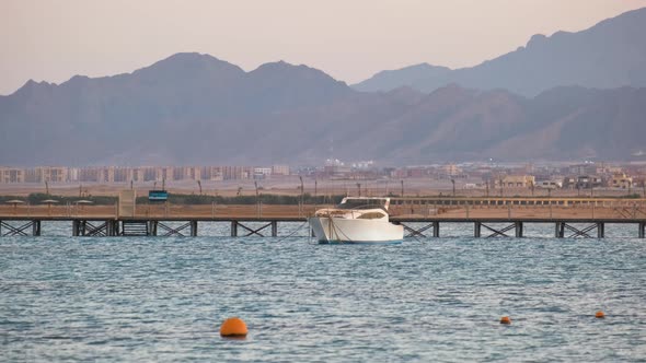 Seascape with Ripple Surface of Blue Sea Water with Distant Yacht at the End of Long Pier Floating alt