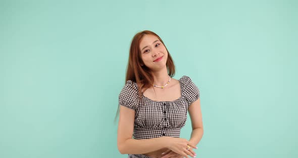 Happy carefree Asian woman dancing and looking at the camera over green background alt
