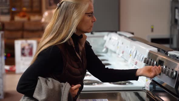 Pretty mature woman turning the knobs on a stove at a kitchen appliance store. alt