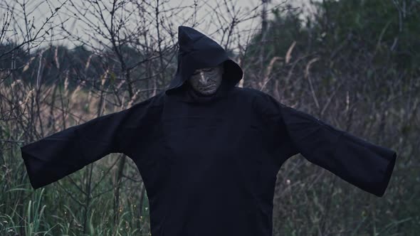 Horror figure in dark costume with hood. Portrait of scary ghost with outstratched arms alt