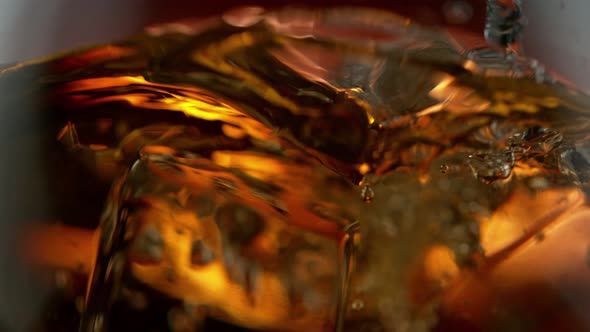 Super Slow Motion Detail Shot of Ice Drop Into Glass with Whiskey at 1000Fps alt