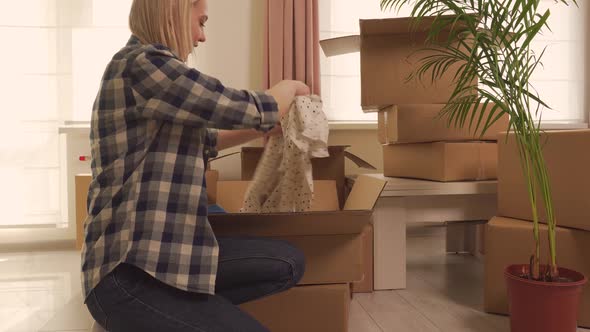 A Young Happy Woman is Sorting Out Boxes of Clothes After Moving in