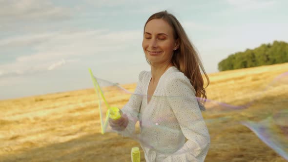Young Woman Runs Around with Huge Soap Bubbles in a Mown Wheat Field alt