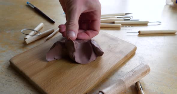 An artist sculpting a project with soft, brown modeling clay using his hands and fingers to shape an alt