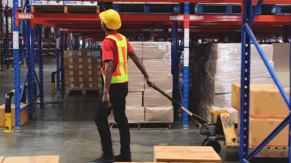 black male warehouse worker pulls a pallet jack with boxes and goods to unload the stock.