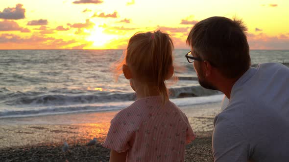 Father and Girl Sit By Sea and Look at Waves and Sunset