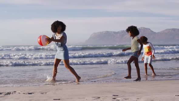African american mother and her children playing with a ball on the beach alt