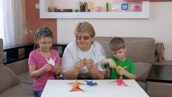 Grandmother with Children Make Paper Cranes in the Room