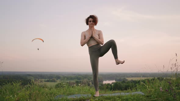 A Young Woman Keeps Her Balance By Doing Yoga Exercises on a Carpet in Nature in the Background a alt