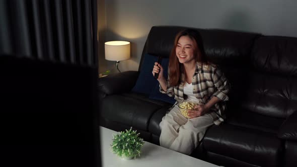 cheerful young woman watching sport TV with arm raised on sofa at night