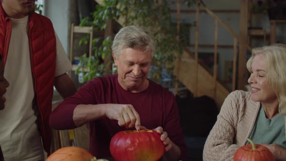 An Elderly Man Sits at the Table and Takes Out the Pulp From the Pumpkin with a Spoon alt