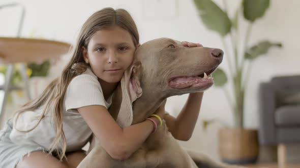 Cheerful Girl Hugging and Stroking Lovely Dog at Home alt
