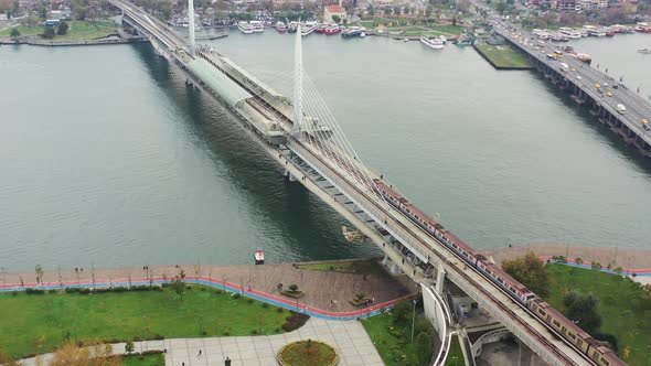 Aerial drone circling the Halic Metro Bridge as a train crosses the Bosphorus River during a cloudy alt