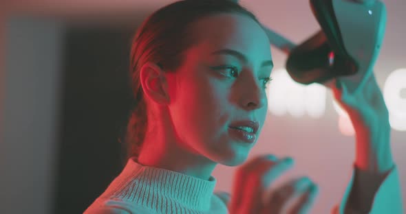 Young woman in neon lights taking off vr goggles and making eye contact with the camera alt