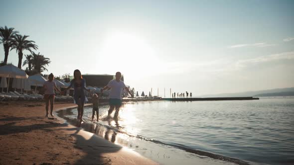 Happy Young Family Have Fun Walking on Beach at Sunset. Family Silhouette Travel Holiday. alt