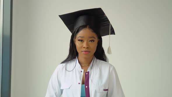 A Young African American Female Graduate in a Master's Hat and White Medical Gown Poses for the alt