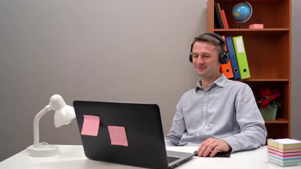 A Young Worker Communicates with a Client at an Online Conference From the Office Through Headphones alt