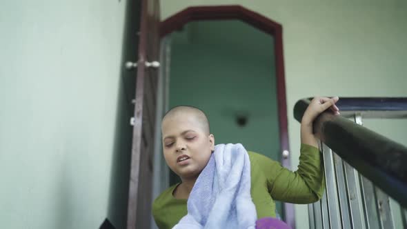 Bald and tired Asian sick young girl sits on the stairs, after Chemotherapy in Cancer, loss of hair alt