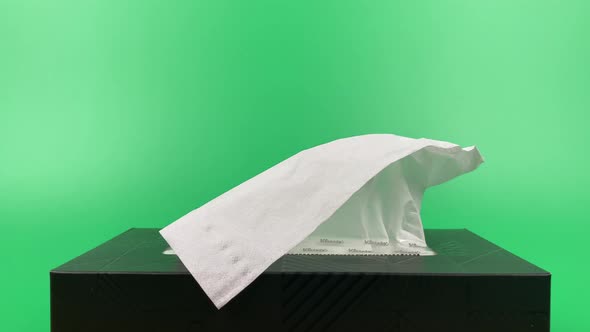 a person's hand pull out a piece of tissue from tissue paper box isolated on green background.