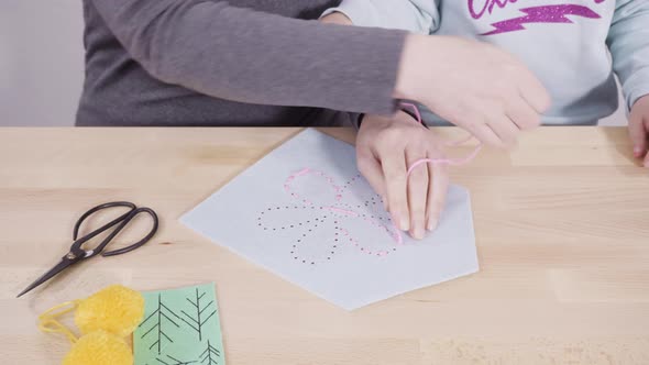 Little girl learning how to sew with her mother at the craft table. alt