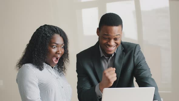 Excited Young Multiethnic African American Colleagues in Formal Wear Happy Looking at Laptop Screen alt