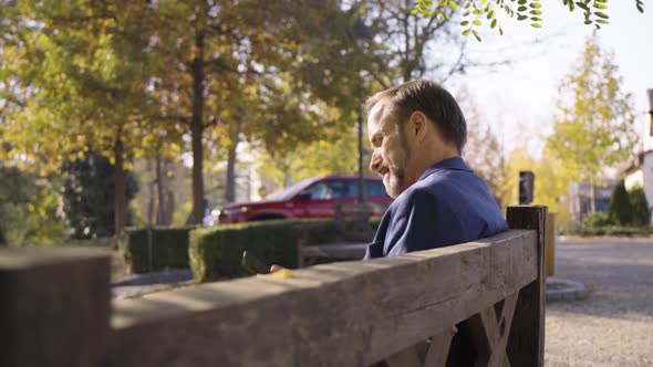 A Middleaged Handsome Caucasian Man Talks on a Smartphone As He Sits on a Bench