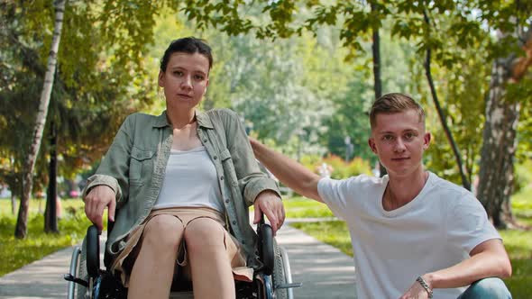 A Woman in a Wheelchair and a Man Sitting Next to Her in the Park  Looking in the Camera alt