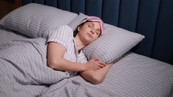 Woman in a Pink Eye Mask Lies Under a Blanket in a Bed and Suffers From Insomnia alt